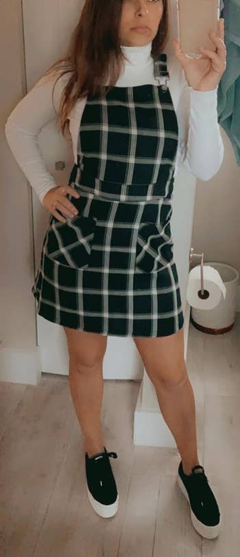 a reviewer wearing the suspender dress in green with a white plaid print 