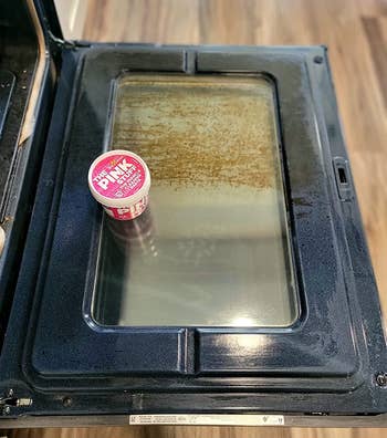 reviewer photo of a tub of the pink stuff on an oven door, half of which is dirty, and half of which is clean