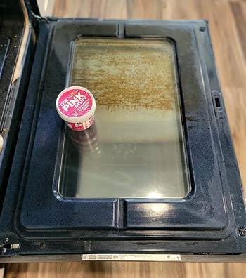 reviewer photo of a tub of the pink stuff on an oven door, half of which is dirty, and half of which is clean
