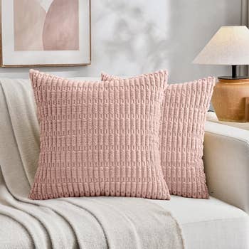 Two textured pillows connected  a pick  sofa with a propulsion  blanket, adjacent  to a lamp and partition  art, creating a cozy and inviting surviving  country   setting