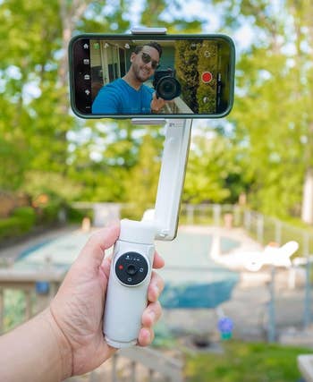 A reviewer holding a phone clipped into a white handled stabilizer 