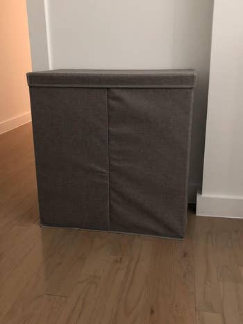 Fabric-covered rectangular storage bin against a wall on a wooden floor