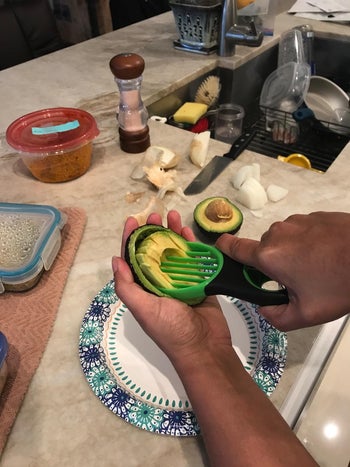 hands hold avocado and the same tool while removing pit from avocado
