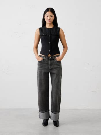 Model successful tailored vest and wide-leg rolled jeans stands confidently with hands successful pockets
