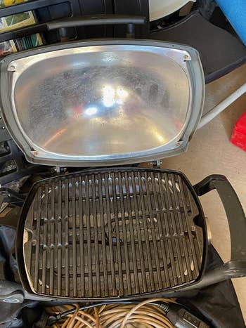 A portable indoor grill with a cleanable lid and utilized grill grates, surrounded by assorted household items
