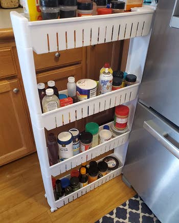 reviewer photo of the white organizer holding various cooking ingredients pulled out next to a fridge