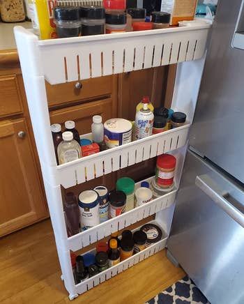 reviewer photo of the white organizer holding various cooking ingredients pulled out next to a fridge