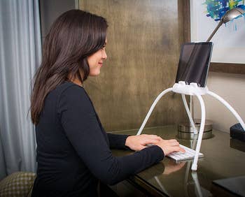 model sitting at a desk with the tablet propped up on the desk with the stand