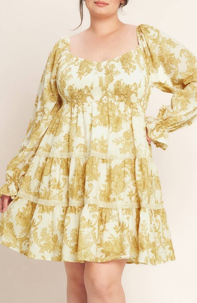 Model in a floral tiered dress with long sleeves poses with one hand on hip, showcasing the outfit's design