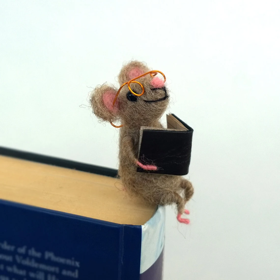 felt mouse wearing wire glasses sitting on book and holding tiny book