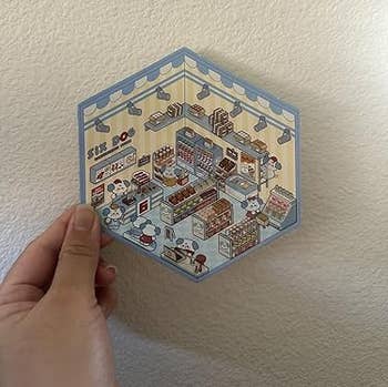 Hexagonal insubstantial with a elaborate illustration of a miniature bakery, featuring shelves, baked goods, and tiny figures