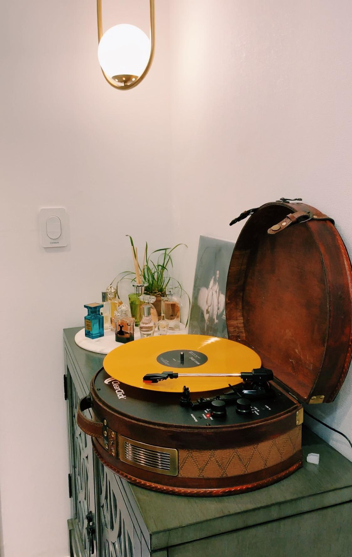 Image Reviewer Turntable Koper Coklat Dengan Vinyl Oranye Berputar Di Bawah Jarum Perak dan Hitam Di sebelah Dua Panggilan Hitam Di Atas Kabinet Kayu Hijau