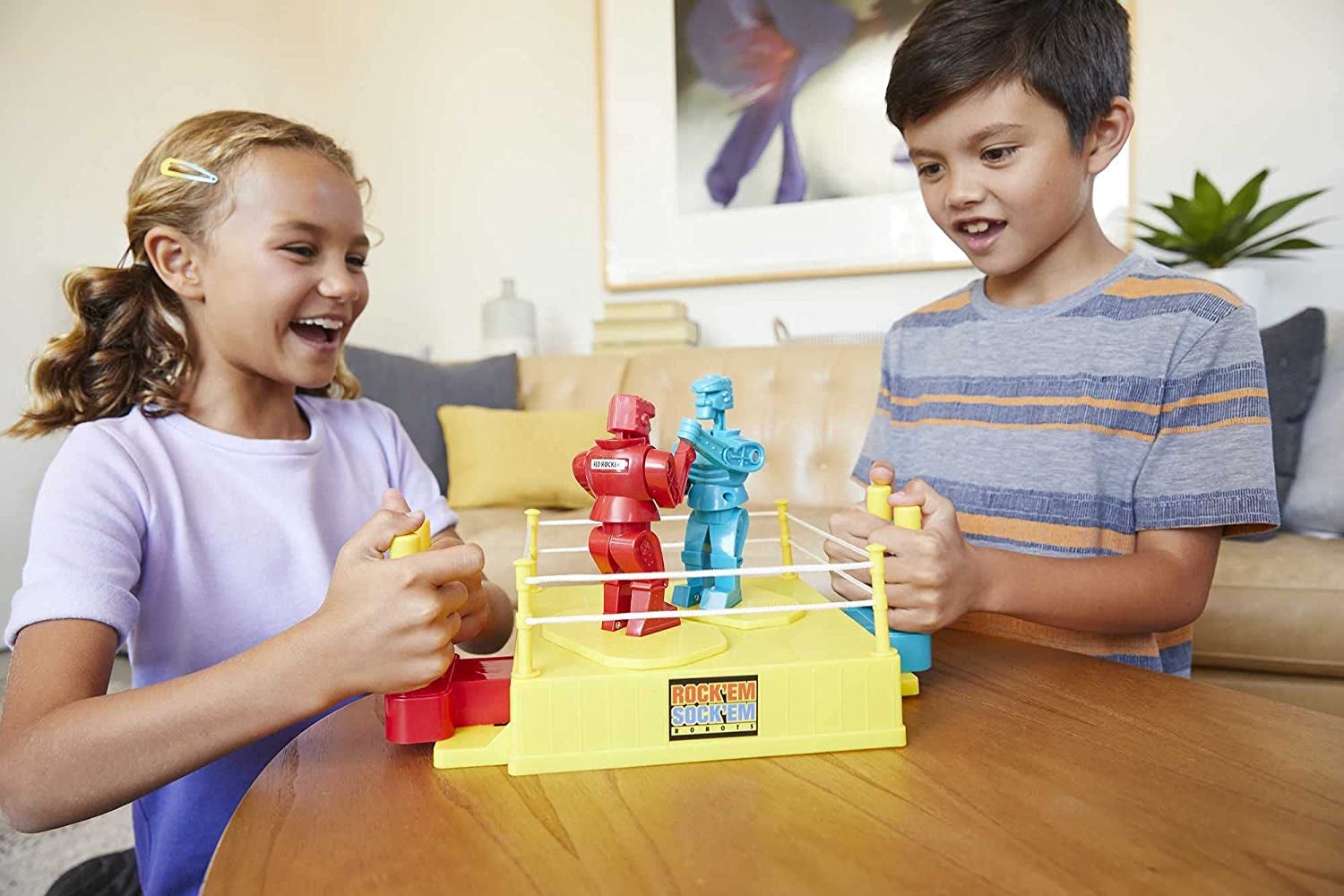 Child models playing with red and blue robots inside yellow boxing ring