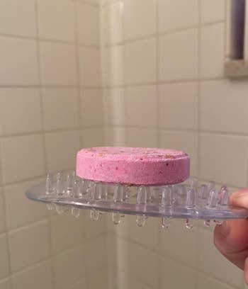 A pink shower steamer on a clear, spiked soap dish in a tiled shower area