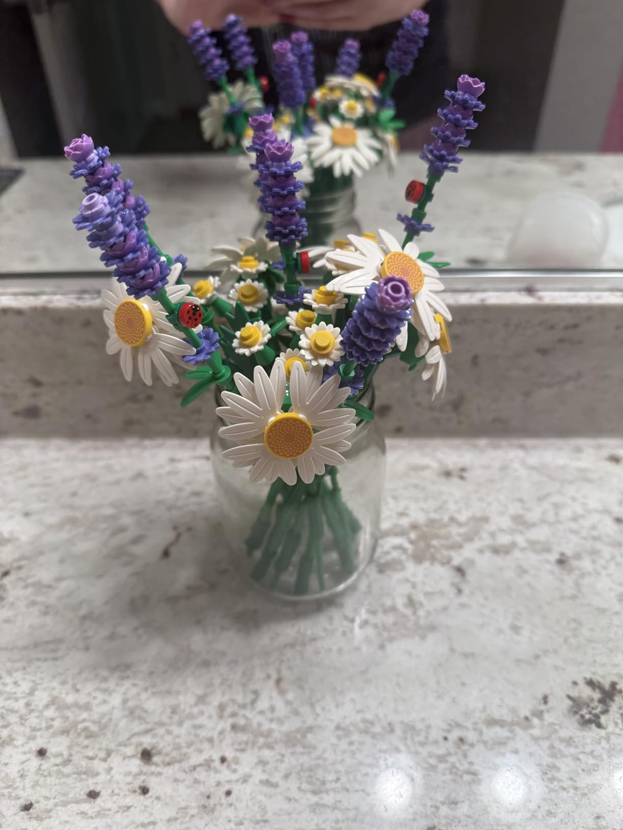 A solid  vase holds LEGO flowers, including daisies and lavender, displayed connected  a bath  antagonistic  with a reflector  reflection