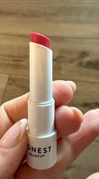 Hand holding a conduit  of Honest Beauty® lipstick with a pinkish  shadiness  visible