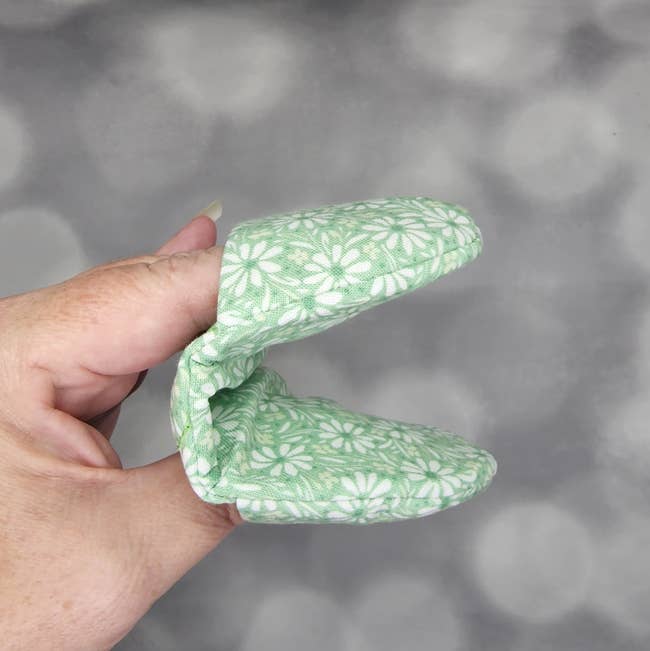 Model wearing the small mitt in green and white flowers that just covers the fingers and thumb 