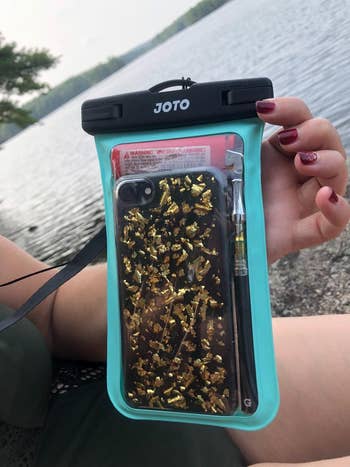 reviewer holding up the teal pouch with their phone in it in front of a body of water