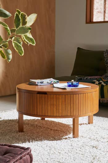 Round wooden table in a cozy living room, adorned with books and decor items, placed on a white shag rug