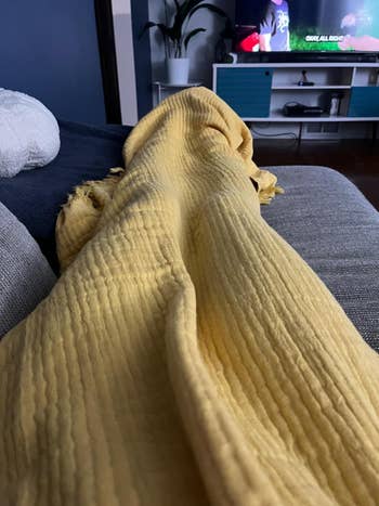 Person lounging connected  a couch, covered with a textured blanket, TV successful  the background. Cozy location  setting