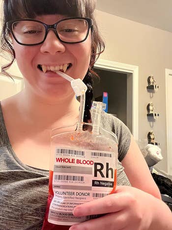 A reviewer with fake fangs drinking from the blood bag