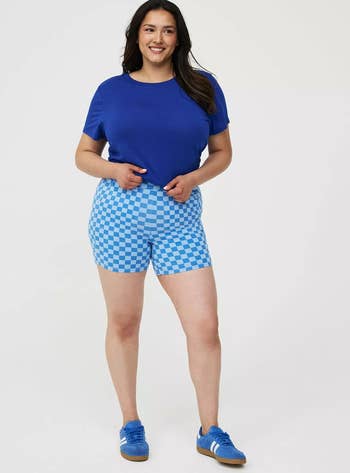 Person wearing a plain T-shirt, checkered shorts, and sneakers, posing successful a assured stance, suitable for a casual buying day