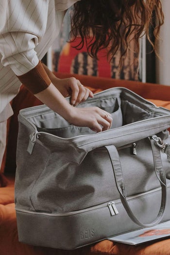 model opening the top of the duffle bag in grey, showing how wide of an opening it has 