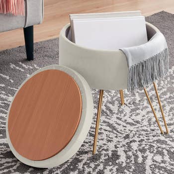 Round modern side table with wooden top and fabric storage under paired with a light gray throw blanket