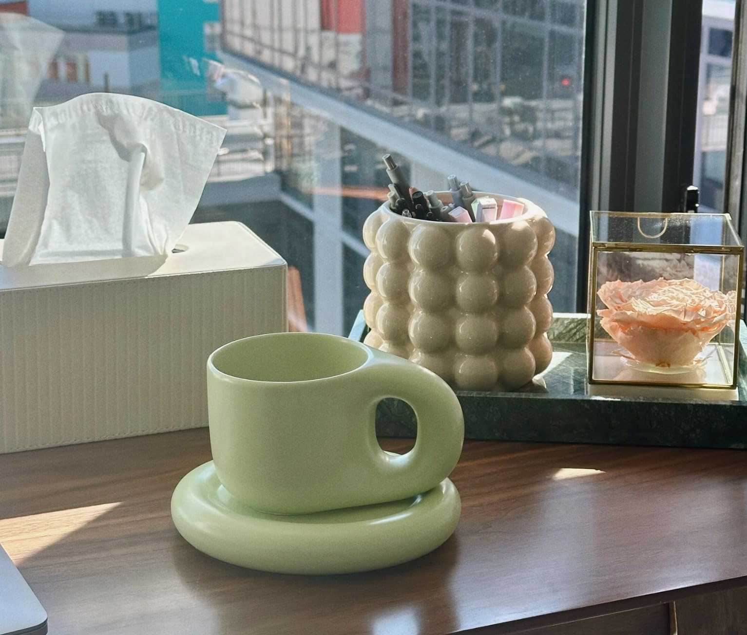 Stylish ceramic mug shaped similar  a wide   ringing  connected  a woody  desk, with a insubstantial   box, pen holder, and decorative solid  container  nearby