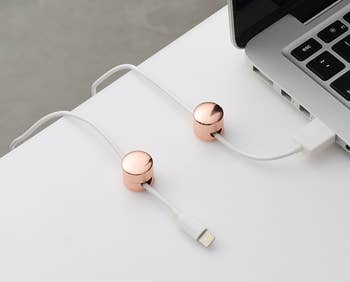 Two rose gold cable organizers on a desk, holding a white charging cable next to a laptop