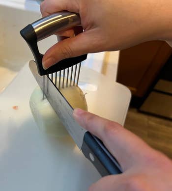 A person chopping an onion using an onion slicer on a white cutting board