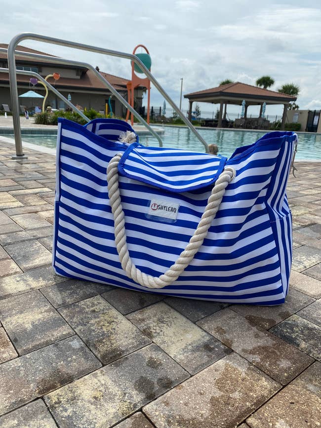 Striped beach bag with rope handles on poolside pavement, perfect for summer outings