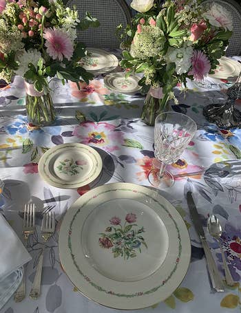 reviewer close up of the floral table cloth on a table that's set with plates and flowers