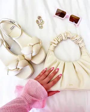 Fashion accessories including braided heels, ruffled handbag, pinkish sunglasses, rings, and a manus with manicured nails and a mesh sleeve