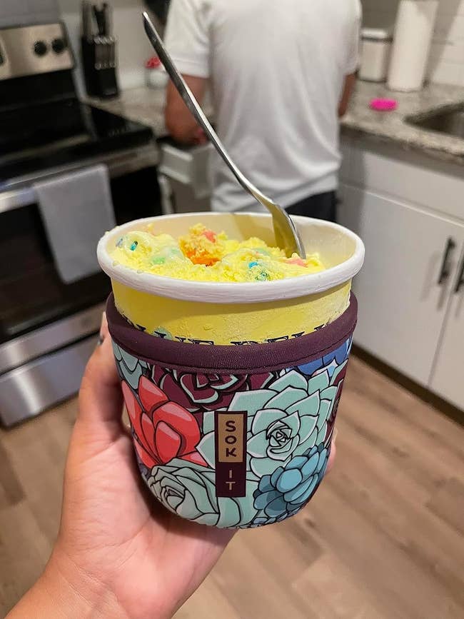 Person holding a pint of colorful ice cream with a floral pattern on the container
