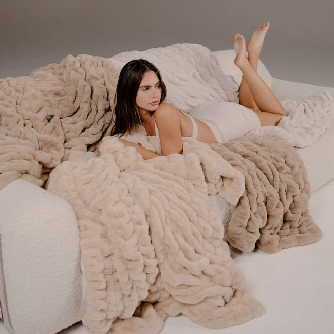 A pistillate   lounges connected  a couch, surrounded by plush faux fur blankets, wearing a comfy  loungewear set