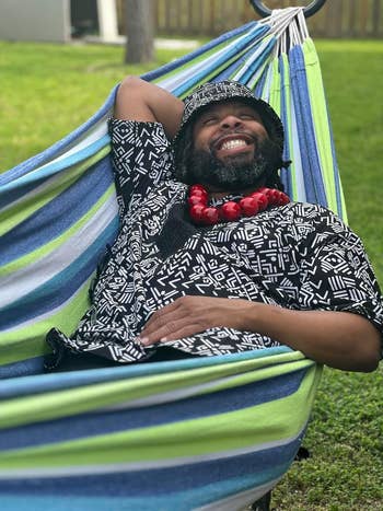 Person relaxing successful a hammock, wearing a patterned garment and bucket hat, with a ample beaded necklace. Perfect for outdoor leisure buying features