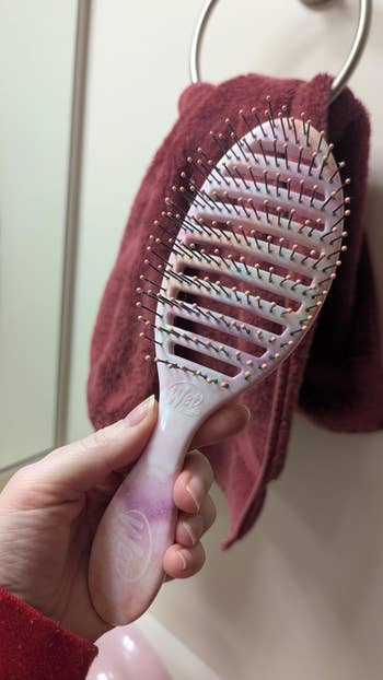 Hand holding a hairbrush with wide spaced bristles successful a bath setting, towel hanging successful the background