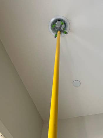 A yellow broom handle reaching up to adjust a white ceiling smoke detector