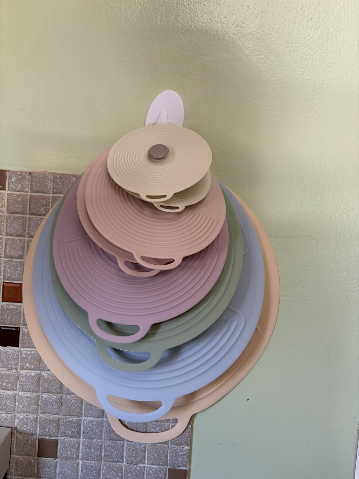 Stacked silicone cookware  lids successful  assorted  sizes bent  connected  a wall-mounted holder, showcasing space-saving room  organization