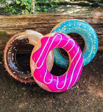Three inflatable donut tubes with chocolate, pinkish  frosting, and bluish  prima  designs are arranged against a log successful  a wooded area