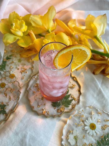Iced pinkish  portion  with an orangish  portion    garnish connected  floral coasters, surrounded by yellowish  flowers, creating a refreshing and elegant scene
