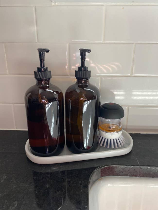 Two brownish  pump bottles connected  a room  antagonistic  with a crockery  brushwood  and soap dispenser, each  neatly arranged connected  a tiny  tray