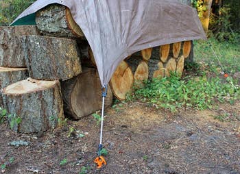 the ground screw anchoring a tarp over a pile of wood 