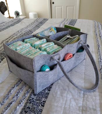 Gray fabric diaper caddy with pockets, filled with diapers and baby care items on a bed