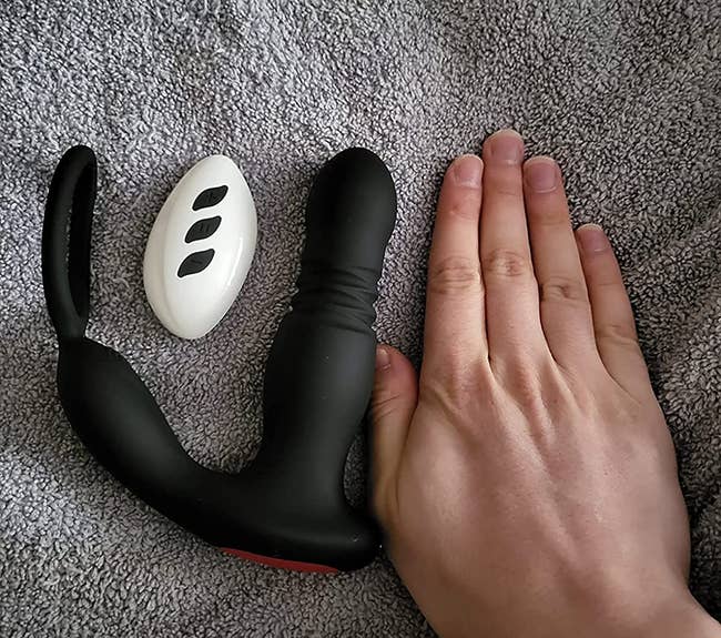 Hand next to black thrusting prostate massager and white wireless remote