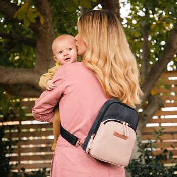 a model holding a baby and wearing a black and tan sling bag