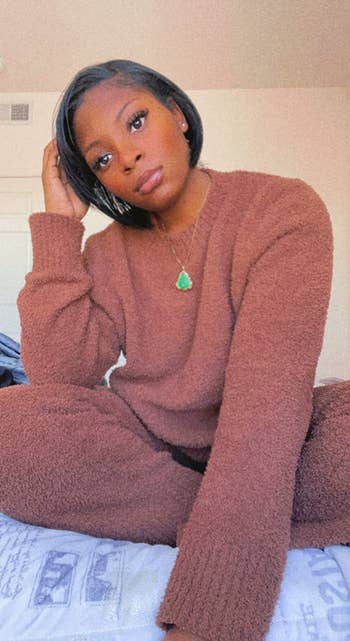 Person sitting connected  a furniture  wearing a cozy knit sweater and pants, accessorized with a necklace