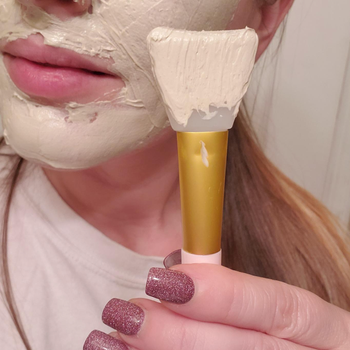 reviewer holding applicator brush with face mask on their face and brush