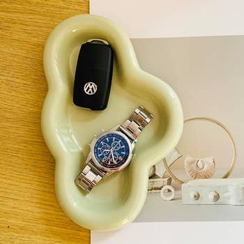 A car key, wristwatch, and jewelry on a decorative tray, showcasing personal accessories